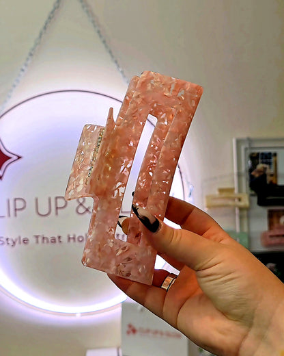 Emily XL claw clip in pink and clear held up close, showing the double-spring hinge and translucent acetate