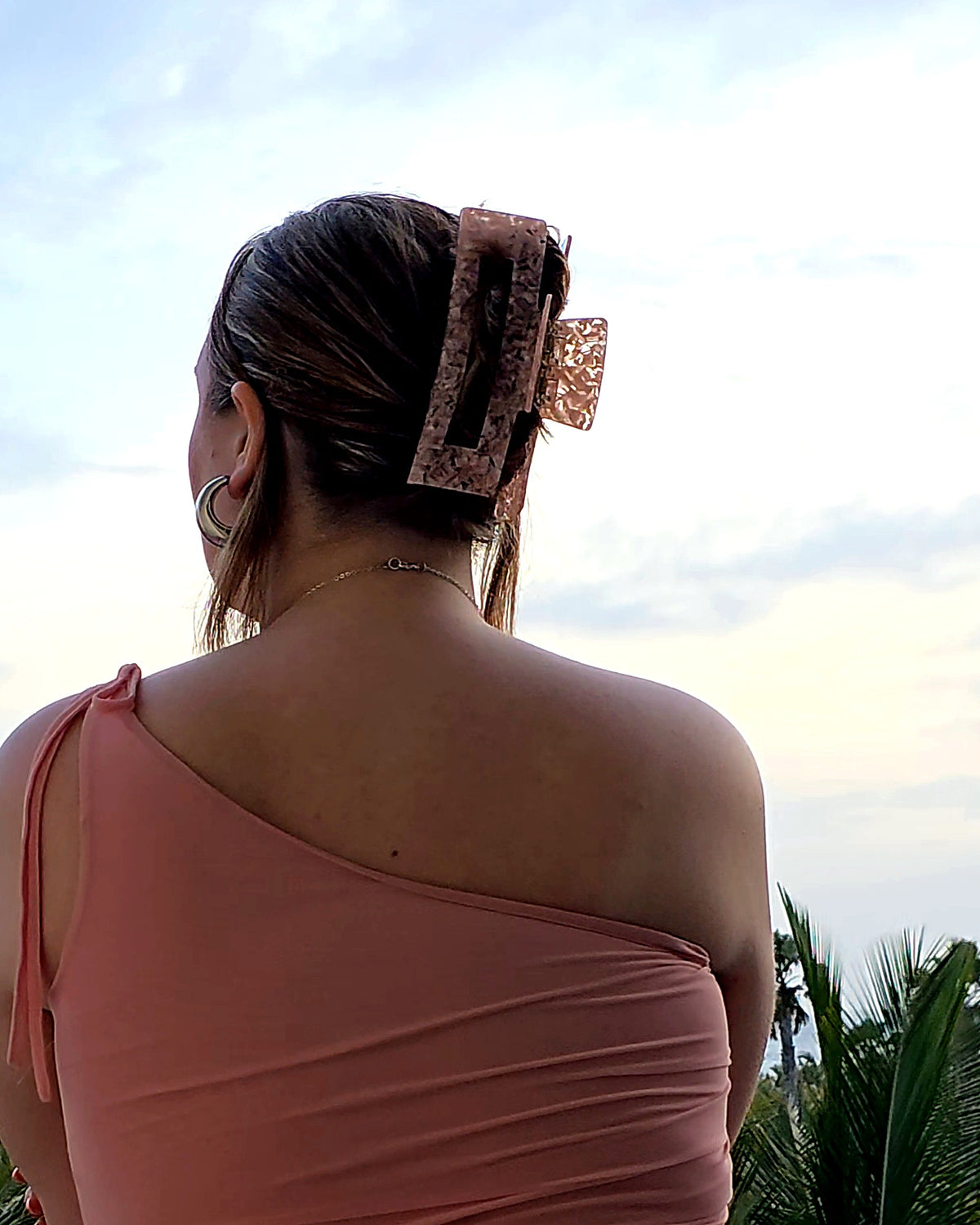 Emily XL claw clip in pink and clear worn in an updo, seen from behind against a sunset sea view