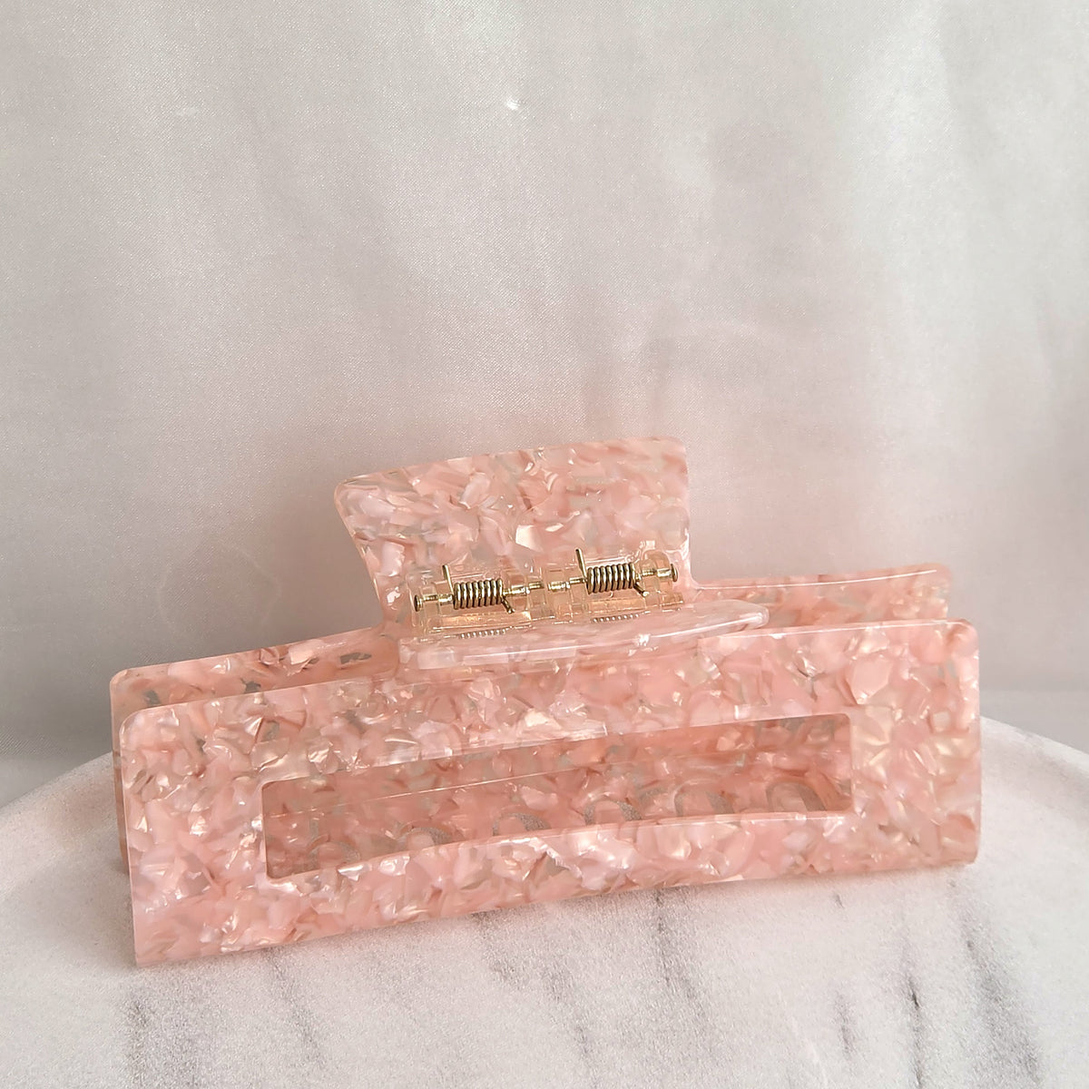 Emily XL claw clip in soft pink speckled acetate, standing on a white marble surface