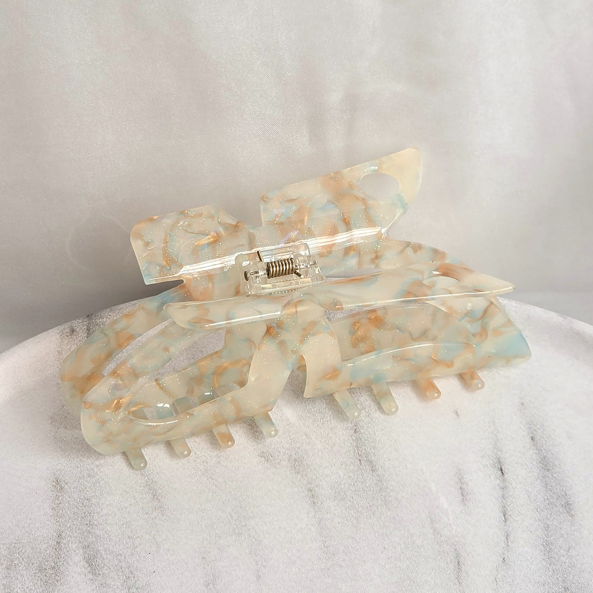 Ruby XL claw clip in clear acetate with warm copper glitter flecks, resting on a white marble surface