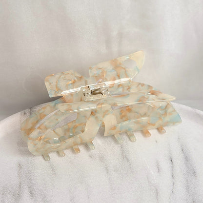 Ruby XL claw clip in clear acetate with warm copper glitter flecks, resting on a white marble surface